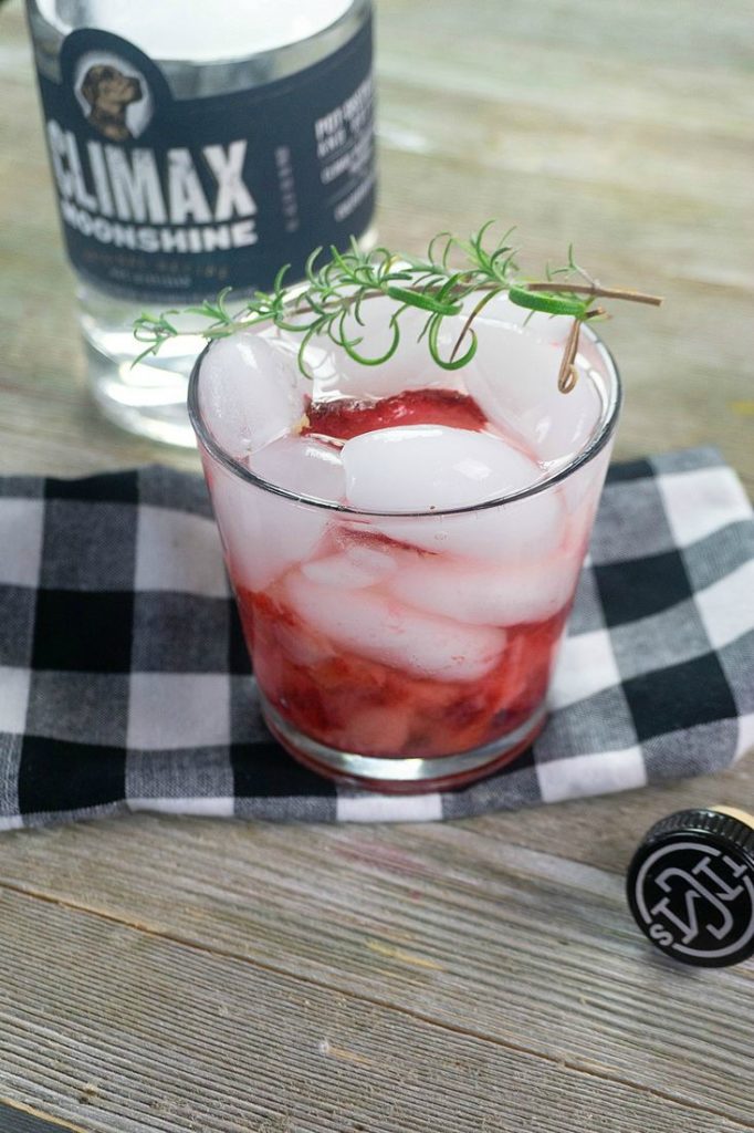 Strawberry Rosemary Moonshine in glass with strawberries, ice, and topped with a rosemary sprig