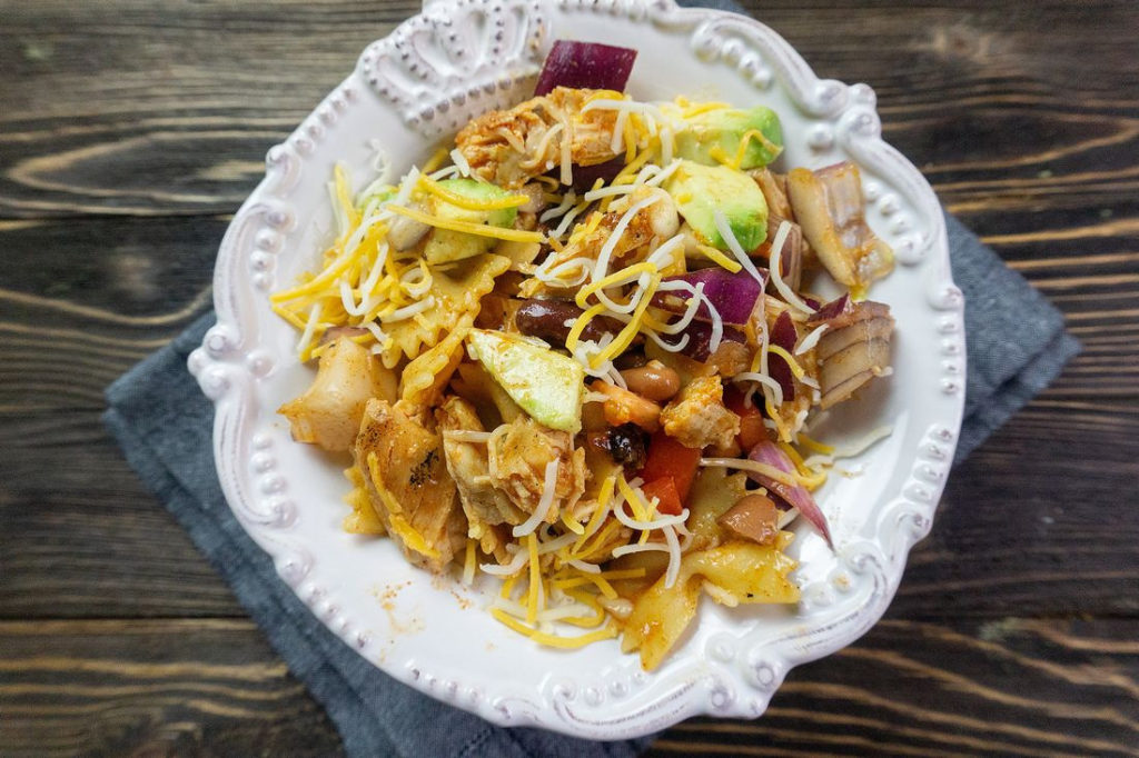 Cast iron boneless chicken tenders, with bow-tie pasta, chili beans, avocados, diced tomatoes, red onions, and cheese 