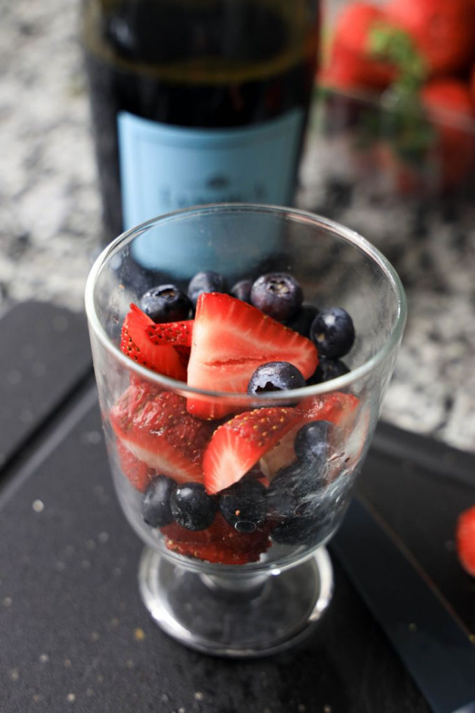 Strawberries and Blueberries in a glass with a bottle of Prosecco next to it.