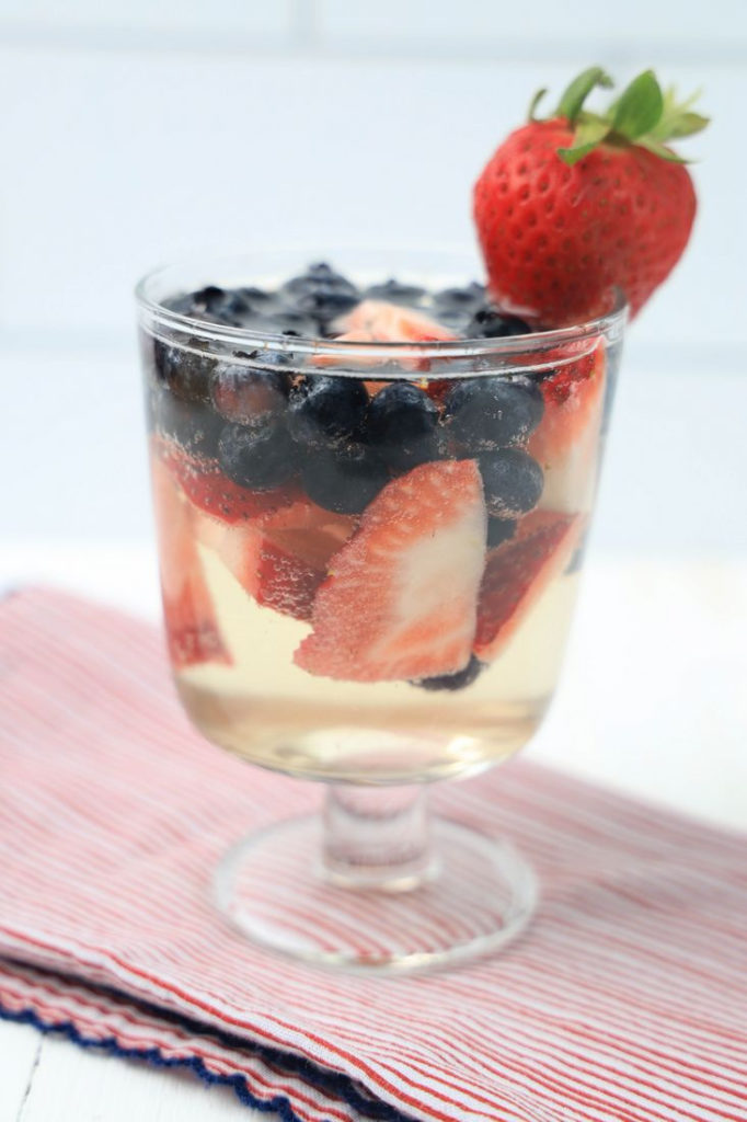 Prosecco with fresh sliced strawberries and blueberries in a cocktail glass.